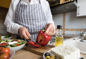 Woman prepare fresh greek salad in the kitchen .