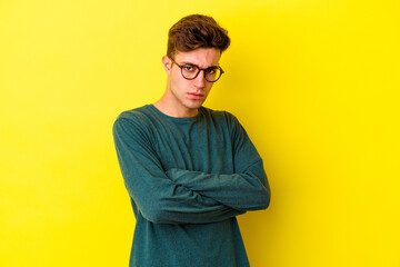 Young caucasian man isolated on yellow background frowning face in displeasure, keeps arms folded.