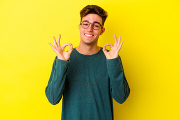 Young caucasian man isolated on yellow background cheerful and confident showing ok gesture.