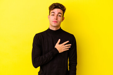 Young caucasian man isolated on yellow background taking an oath, putting hand on chest.