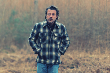 Man in checkered coat in rainy woodland.