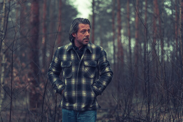 Fototapeta na wymiar Middle aged man with stubble beard in a checkered coat in a rainy forest.