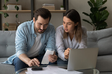 Couple calculating domestic bills, planning budget together, using laptop and calculator, married...