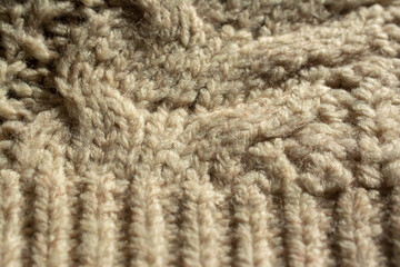 Close-up of a large knitted jumper. Ribbed edge knitting and central twist. Beige, natural colour.