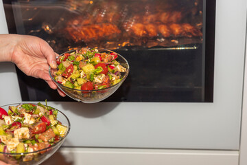 Close up view of woman holding two salad bowls on pork ribs in oven.
