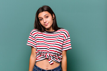 Young Indian woman isolated on blue background shrugs shoulders and open eyes confused.