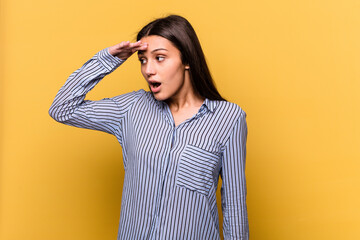 Young Indian woman isolated on yellow background looking far away keeping hand on forehead.