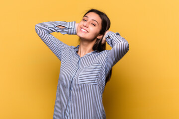 Young Indian woman isolated on yellow background feeling confident, with hands behind the head.