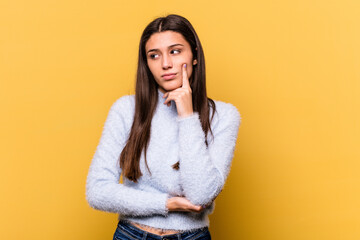 Young Indian woman isolated on yellow background contemplating, planning a strategy, thinking about the way of a business.