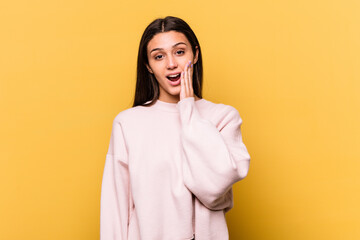 Young Indian woman isolated on yellow background shouts loud, keeps eyes opened and hands tense.