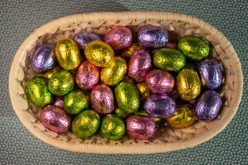 multicoloured chocolate easter candies in a basket on a green background
