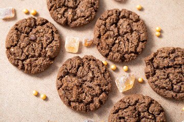 Chocolate granola cookies with brown cane sugar, spread out on a beige cardboard background. Chocolate chip cookies sweet snack