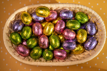 multicoloured chocolate easter candies in a basket on a yellow background
