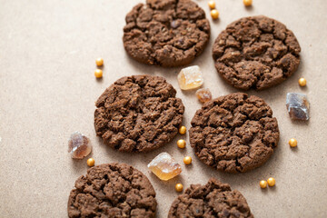 Aromatic chocolate granola cookies with brown cane sugar, spread out on a beige cardboard background. Chocolate chip cookies sweet snack