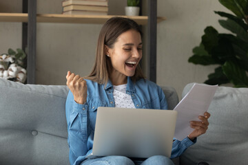 Close up overjoyed woman reading good news in paper letter sitting on couch with laptop on laps at...