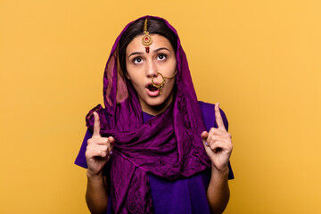 Young Indian woman wearing a traditional sari clothes isolated on yellow background pointing upside with opened mouth.