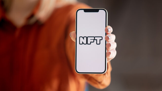Wroclaw, Poland - 20 March 2021: woman holding iPhone 12 with NFT (Non-fungible token) logo on the screen