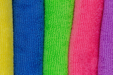 Towels and cleaning cloths in different colors as background to the topics household, showers and hygiene with the colors blue, yellow and pink
