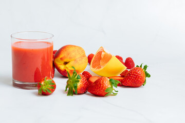 Red smoothie in a glass next to apricot, strawberries, grapefruit and raspberries. Red juice from fresh fruits. Healthy juice for breakfast. 