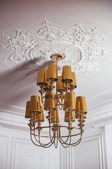 Beautiful luxury golden chandelier hanging on the ceiling with white mouldings in living room