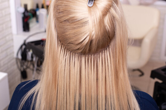 Professional blonde hair extension in hairdressing salon. Close-up view of strands and capsules.