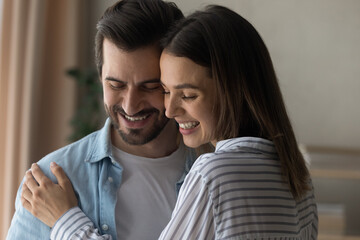 Close up happy woman and man hugging, enjoying tender moment, standing at home, laughing, having fun, husband and wife embracing, expressing love and care, spending free time together, romantic date