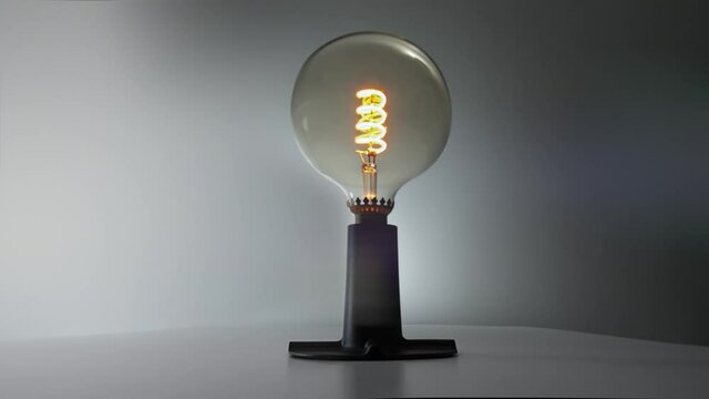 a light bulb with a coiled filament on a black base on a gray background turns on and lights up