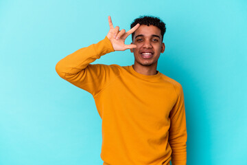 Fototapeta premium Young african american curly man isolated on blue showing a horns gesture as a revolution concept.