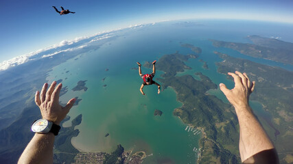 A group of parachuting friends jumping over the sea. First person view.