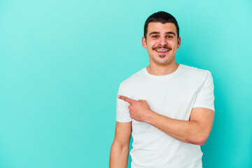 Obraz premium Young caucasian man isolated on blue background smiling and pointing aside, showing something at blank space.