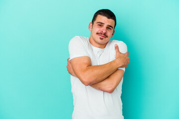 Young caucasian man isolated on blue background hugs, smiling carefree and happy.