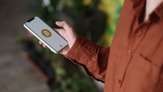 Wroclaw, Poland - 20 March 2021: woman holding iPhone 12 with Bitcoin logo on the screen