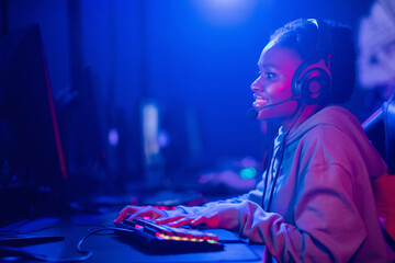 Streamer african young woman rejoices in victory professional gamer playing online games computer with headphones, neon color © Parilov