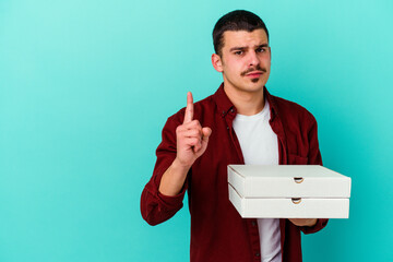 Young caucasian man holding pizzas isolated on blue background showing number one with finger.