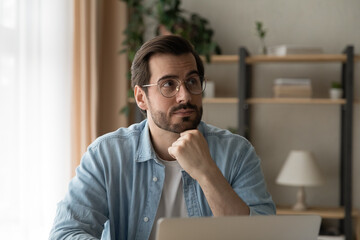 Close up thoughtful businessman wearing glasses looking to aside, distracted from laptop, touching...
