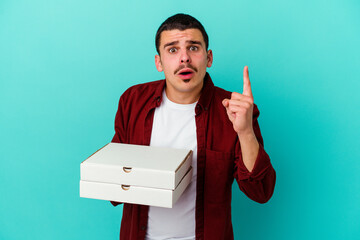 Young caucasian man holding pizzas isolated on blue background having an idea, inspiration concept.