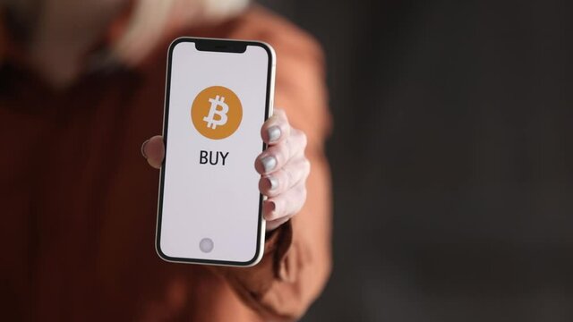 Wroclaw, Poland - 20 March 2021: woman holding iPhone 12 with Bitcoin logo on the screen