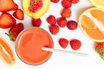 Red smoothie in a glass next to apricot, strawberries, grapefruit and raspberries. Red juice from fresh fruits. Healthy juice for breakfast. 
