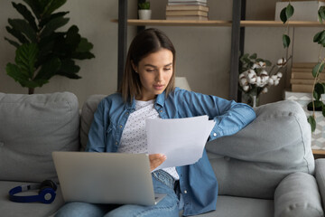 Close up focused woman reading documents, using laptop at home, student freelancer working on...