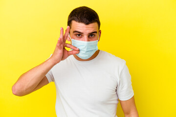 Young caucasian man wearing a protection for coronavirus isolated on yellow background with fingers on lips keeping a secret.