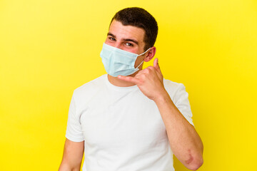 Young caucasian man wearing a protection for coronavirus isolated on yellow background showing a mobile phone call gesture with fingers.