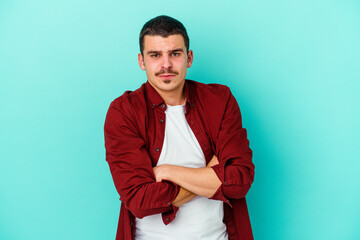 Young caucasian man isolated on blue background frowning face in displeasure, keeps arms folded.