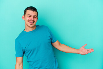 Young caucasian man isolated on blue background showing a welcome expression.