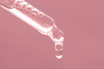 Closeup of pink dropper, falling drop close up. Beauty skin care product. Pipette with essential...