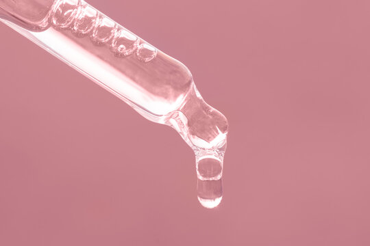 Closeup of pink dropper, falling drop close up. Beauty skin care product. Pipette with essential oil, serum with peptides, hyaluronic acid on pink background. Self care concept