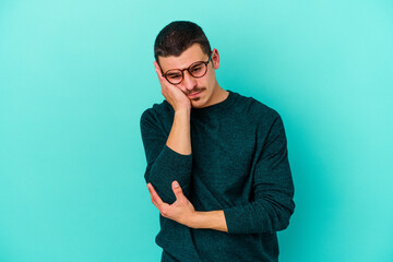 Young caucasian man isolated on blue background who is bored, fatigued and need a relax day.