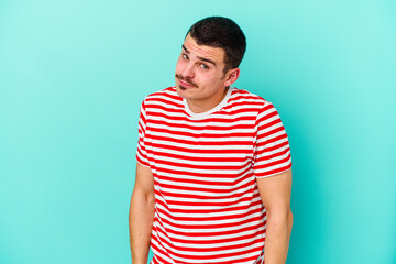 Obraz premium Young caucasian man isolated on blue background shrugs shoulders and open eyes confused.