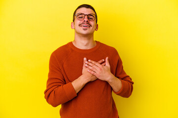 Young caucasian cool man isolated on yellow background has friendly expression, pressing palm to chest. Love concept.