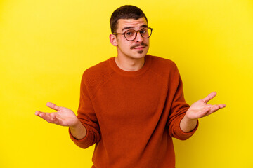 Young caucasian cool man isolated on yellow background doubting and shrugging shoulders in questioning gesture.