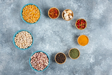 Bunch of spices and bowls of beans, corns on marble background